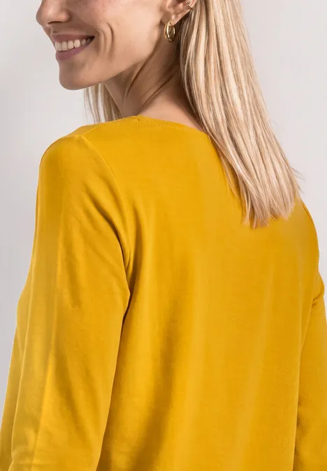3/4-Arm Shirt mit U-Boot-Ausschnitt saffron yellow Frau mit blondem Haar, Rückenansicht, trägt senfgelben Pullover und lächelt.