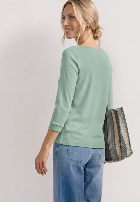 Eine Frau von hinten mit hellgrünem Pullover, Jeans und gestreifter Tasche über der Schulter.