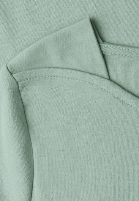 Nahaufnahme eines mintgrünen Baumwollshirts mit überlappendem Rundhalsausschnitt und Ziernaht.