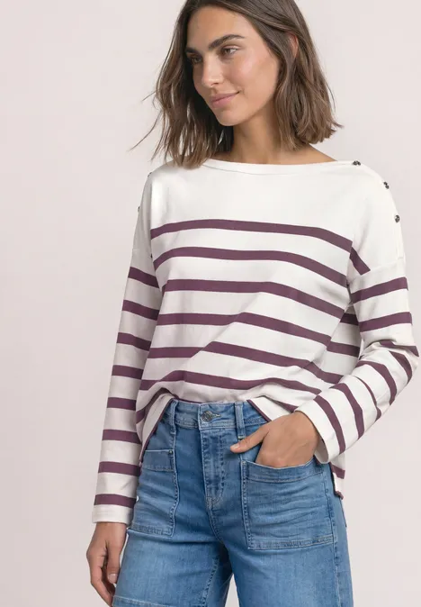 Frau trägt weiß-lila gestreiftes Langarmshirt, blaue High-Waist-Jeans, eine Hand in der Tasche.