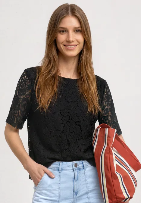 Frau in schwarzer Spitzenbluse und Jeans trägt eine rot-weiß gestreifte Tasche.
