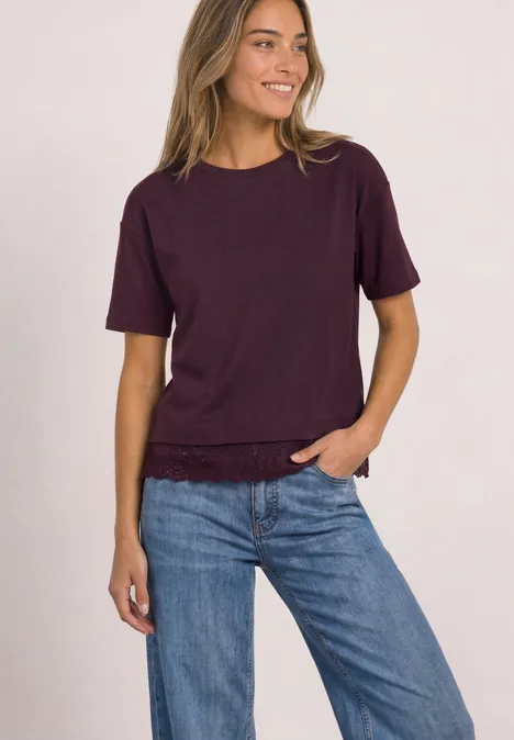 Uśmiechnięta kobieta ma na sobie ciemnofioletowy T-shirt i niebieskie dżinsy.