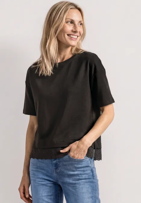 Uśmiechnięta kobieta w czarnym T-shircie i niebieskich dżinsach na jasnym tle.