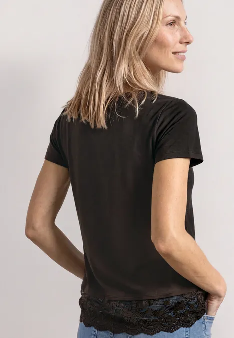 Frau in schwarzem T-Shirt von hinten, lässig die Hände in den Taschen, seitlicher Blick.