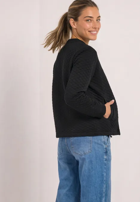 Seitliche Aufnahme einer Frau in schwarzer Steppjacke und blauen Jeans, die über die Schulter lächelt.