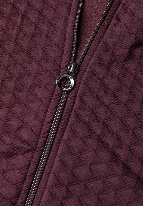 Dunkelrote, gesteppte Jacke mit sichtbar gewebter Struktur und Metallring am Reißverschluss.