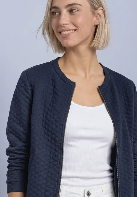 Eine lächelnde Frau trägt eine gesteppte dunkelblaue Jacke und ein weißes Oberteil.