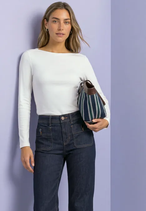 Basic Shirt mit U-Boot-Ausschnitt off white Frau in weißem Langarmshirt und dunkler Jeans hält eine gestreifte Tasche vor violettem Hintergrund.