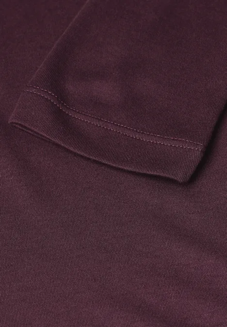 Close-up van een bordeauxrood kledingstuk met een zichtbare zoom en steeknaad.