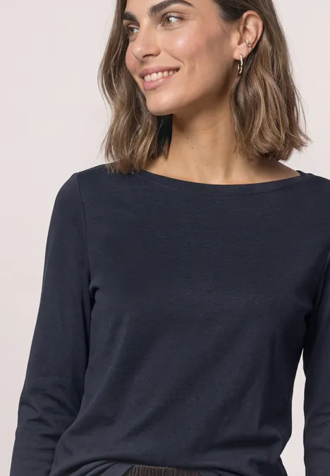 Portrait d'une femme souriante en t-shirt à manches longues bleu marine, mi-corps, regard vers la droite.