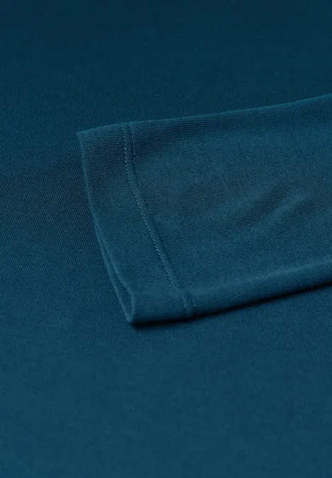 Haut basic a col bateau blue petrol Nahaufnahme eines petrolblauen T-Shirt-Ärmels auf glatter Oberfläche.