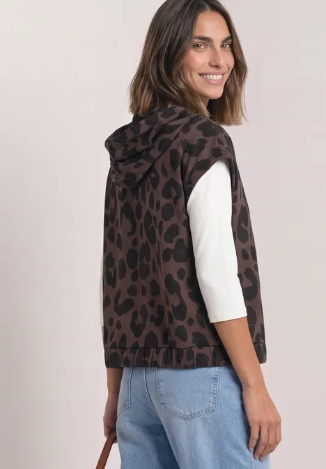 Weste mit Kapuze und Print molten earth Frau in braun-schwarzem Leo-Kapuzenpullunder über weißem Shirt und Jeans, blickt lächelnd über die Schulter.