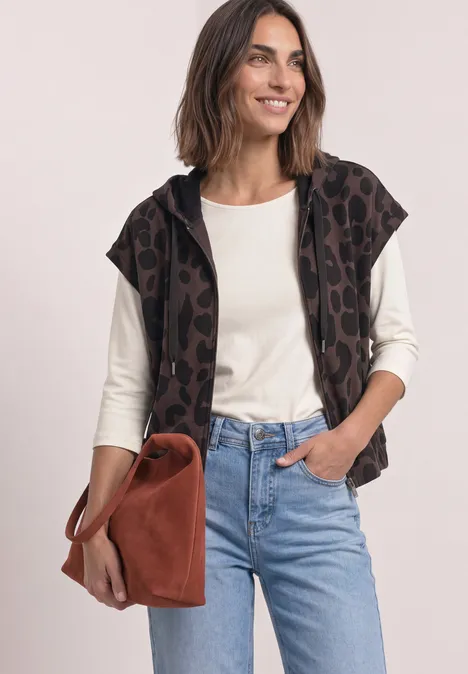 Weste mit Kapuze und Print molten earth Frau in Jeans, weißem Langarmshirt, Leopardenweste mit Kapuze und brauner Wildledertasche, lächelnd.