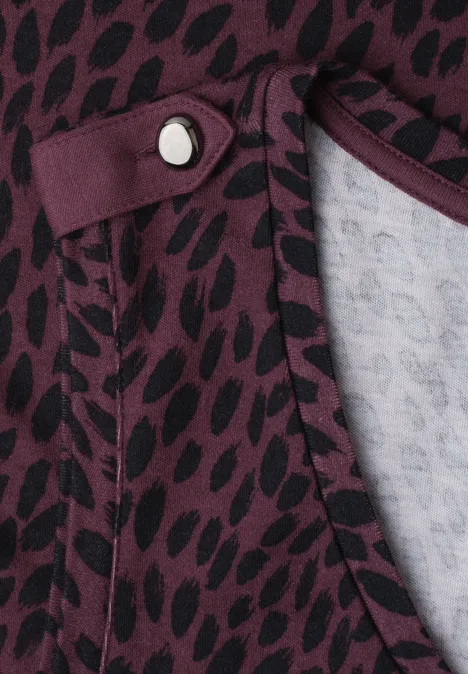 Close-up van een paars shirt met zwart stippenpatroon en decoratieve knoop bij de hals