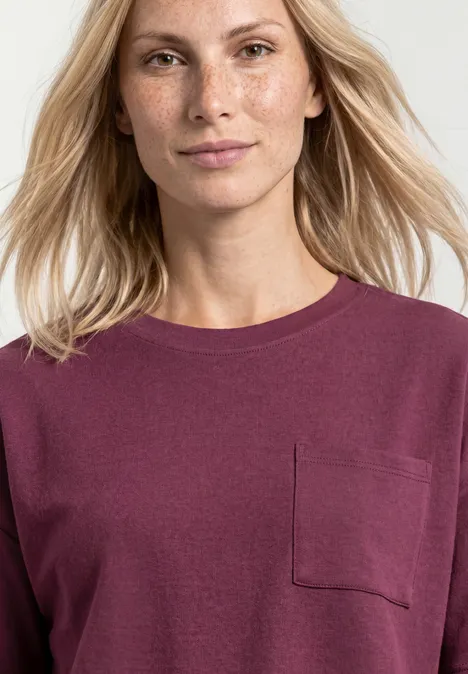Portrait d’une femme blonde portant un pull bordeaux avec poche poitrine sur fond clair.