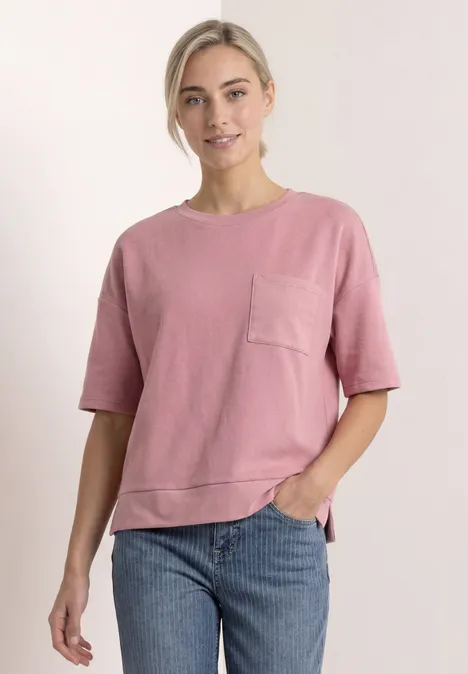 Shirt met ronde hals en structuur vintage blush Vrouw in loszittend roze T-shirt met borstzak en spijkerbroek, staand voor een lichte achtergrond.