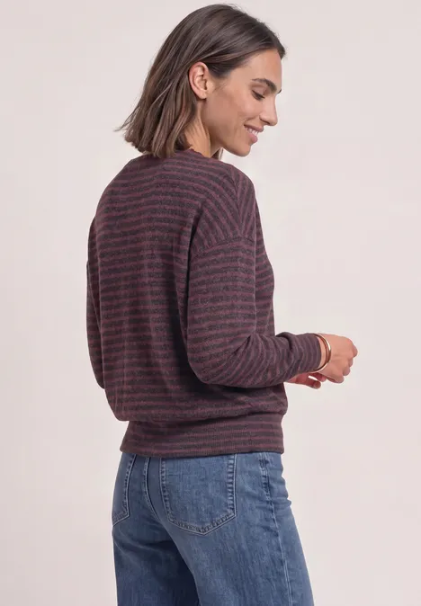 Frau mit gestreiftem Pullover und Jeans, seitlich stehend und lächelnd.