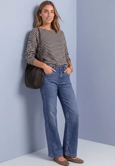 Langarm Shirt mit Elastikbund black coffee mel. Frau steht vor hellblauem Hintergrund, trägt gestreiftes Shirt, blaue Jeans, braune Loafers und schwarze Schultertasche.