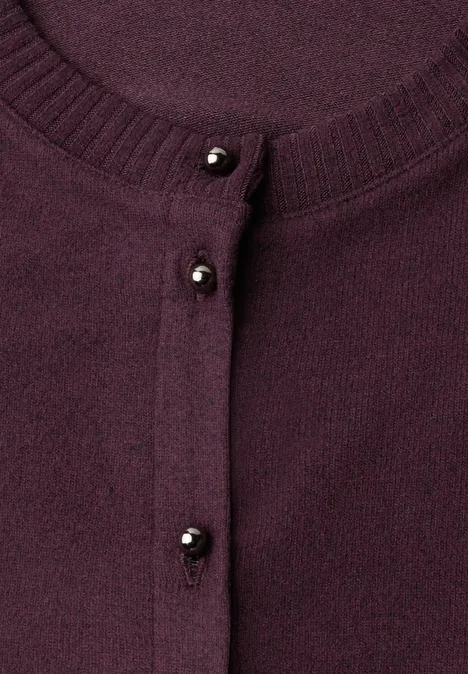 Gros plan sur un gilet violet à petits boutons noirs en perles.