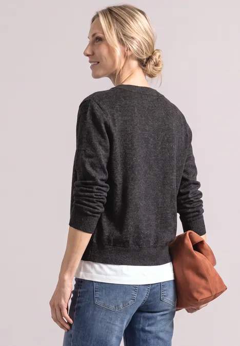 Frau von hinten in schwarzem Pullover, weißem Shirt, blonden Dutt, Jeans, hält eine braune Tasche.