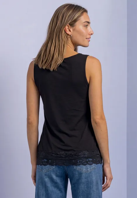 Rückansicht einer Frau in schwarzem ärmellosem Top mit Spitzensaum und blauen Jeans vor hellem Hintergrund.