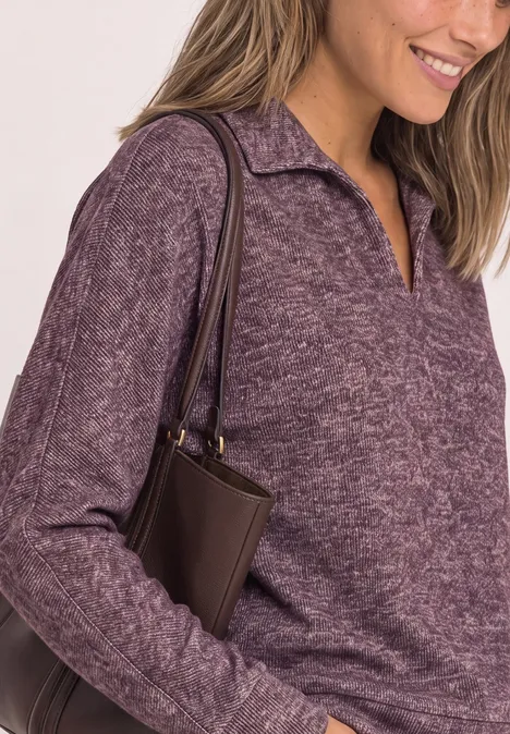 Frau in fliederfarbenem Strickpullover mit dunkelbrauner Schultertasche, lächelt seitlich.