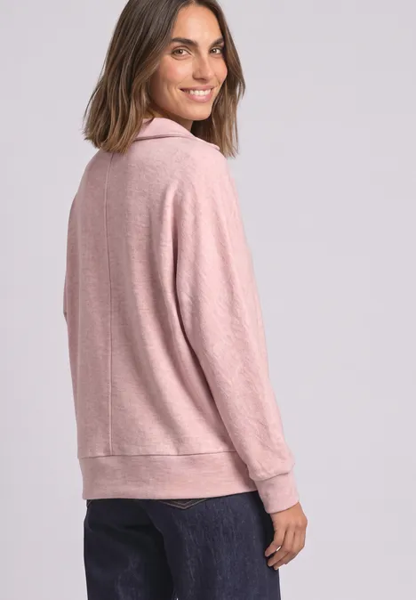 Eine Frau trägt ein rosafarbenes Sweatshirt und schaut lächelnd über die Schulter.