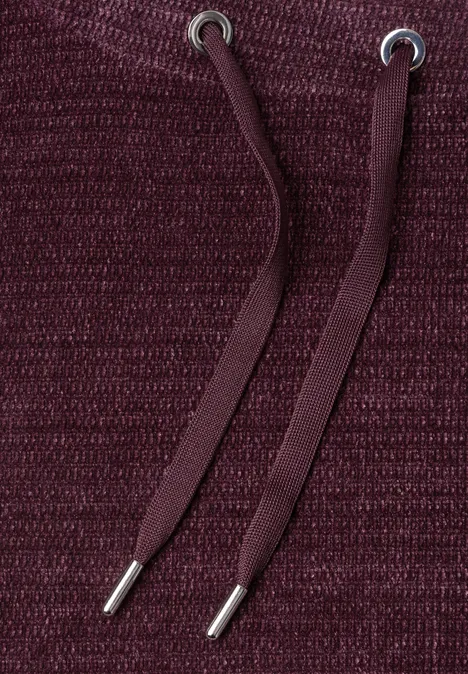 Gros plan sur un tissu tricoté bordeaux avec deux cordons de capuche.