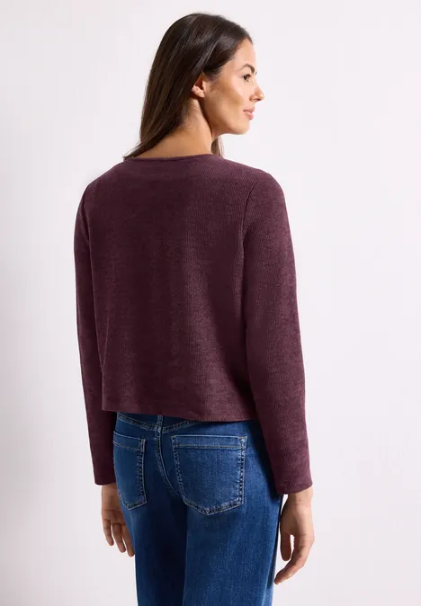 Femme de dos en pull bordeaux et jean bleu, légèrement tournée sur le côté.