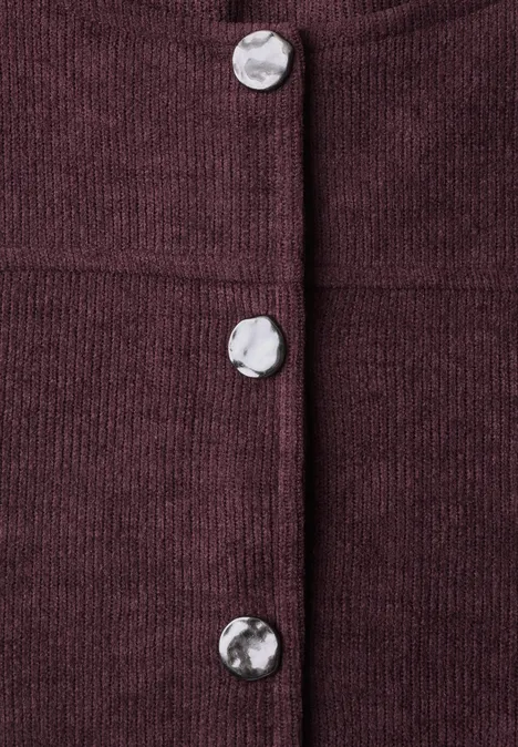 Gros plan sur un tissu en maille bordeaux avec des boutons argentés apparents.