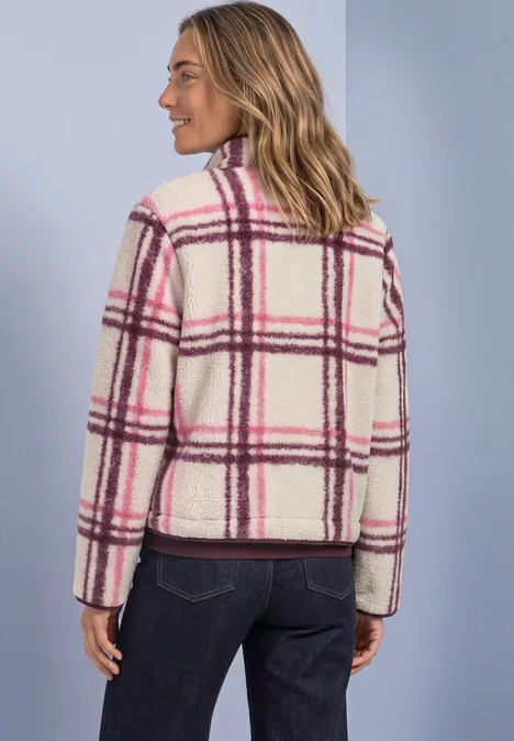 Vrouw draagt witte, zachte geruite jas met roze-paarse strepen, zijaanzicht tegen lichtblauwe achtergrond.
