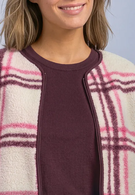 Vrouw draagt een bordeaux top onder een beige fleecevest met roze-paarse ruitprint.