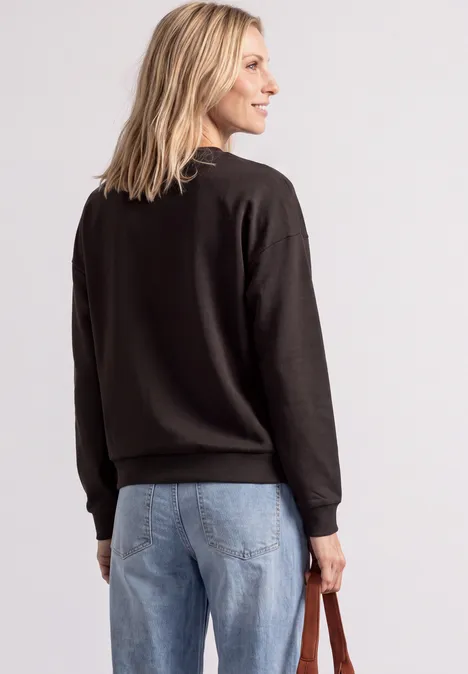 Frau von hinten in schwarzem Pullover und Jeans, hält eine Tasche in der Hand.