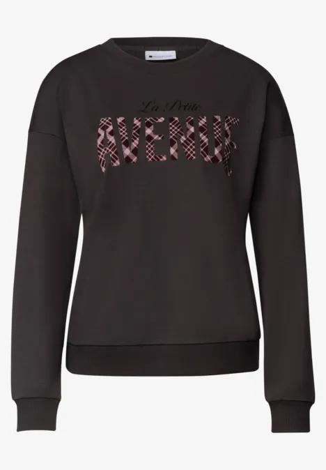 Schwarzer Sweater mit Rundhalsausschnitt und Frontschriftzug "AVENUE" in rot geblümtem Muster.