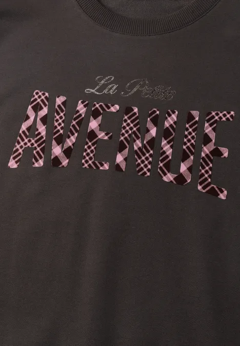 Dunkles T-Shirt mit pink gemustertem Schriftzug 'La Plus AVENUE'.