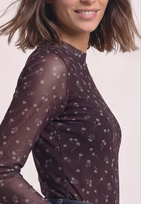 Frau trägt durchsichtiges, langärmeliges Shirt mit zartem Blumenmuster in dunklem Farbton.
