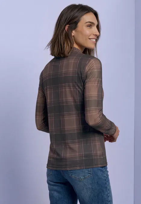 Frau trägt kariertes Langarmshirt und Jeans, steht vor hellem Hintergrund, von hinten.