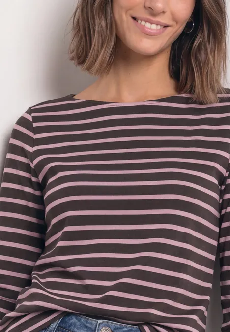 Frau mit schulterlangem Haar trägt ein rosa-dunkelbraun gestreiftes Langarmshirt und lächelt.