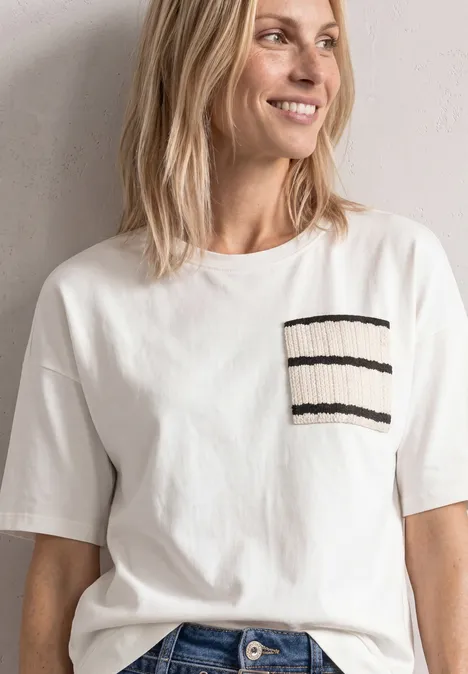 Vrouw in een wit T-shirt met korte mouwen en een borstzak met zwarte strepen, glimlachend.