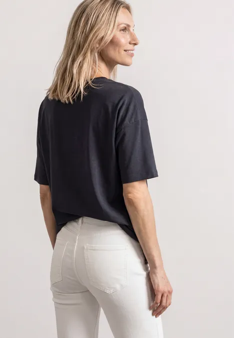 Vrouw in zwart t-shirt en witte spijkerbroek, schuin staand, blik naar links.
