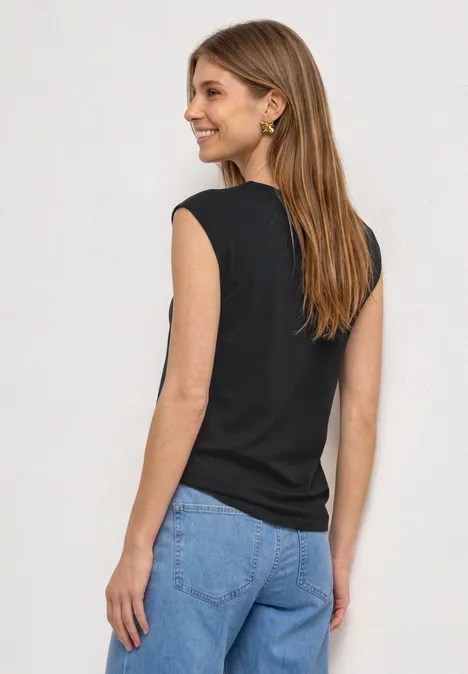 Shirt met afhangende schouders en uitsnijding Black Vrouw van achteren in zwart topje en blauwe spijkerbroek voor neutrale achtergrond.