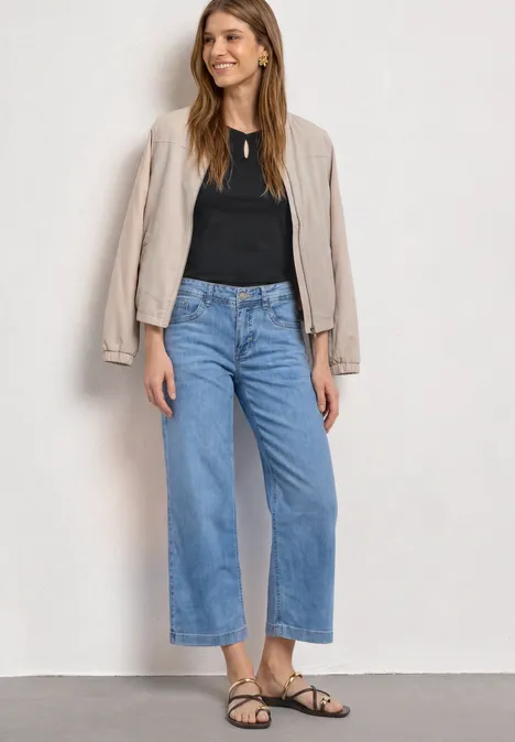 Shirt met afhangende schouders en uitsnijding Black Een vrouw staat voor een witte achtergrond in wijde, blauwe cropped jeans, zwart topje, beige blazer en sandalen.