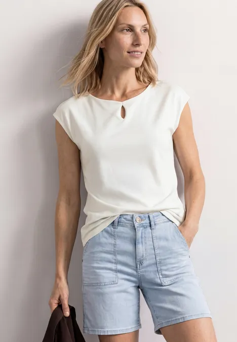 Femme en t-shirt blanc et short en jean clair, style décontracté d’été, mains dans les poches.