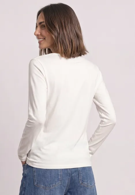 Frau von hinten in weißem Langarmshirt und blauen Jeans vor neutralem Hintergrund.