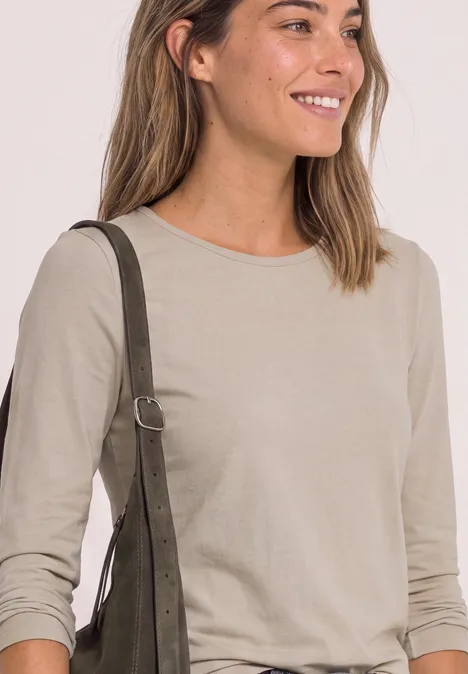 Lächelnde Frau in beigem Langarmshirt mit grüner Schultertasche.