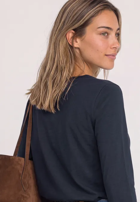 T-shirt basique à manches longues, couleur unie darkest blue Une femme aux cheveux bruns porte un haut noir à manches longues et un sac en daim marron.