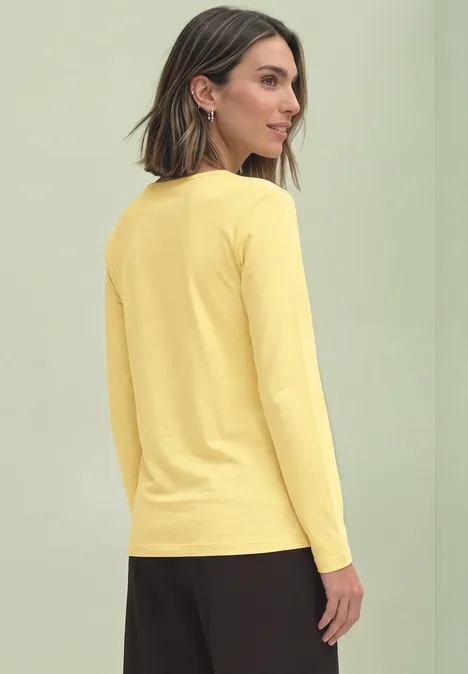 Frau von der Seite in gelbem Langarmshirt vor hellgrünem Hintergrund.