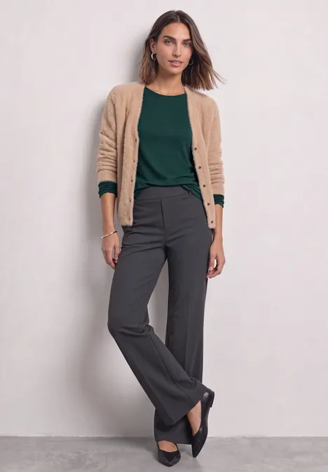 Basic Langarm Shirt in Unifarbe shadow teal Frau trägt beigen Cardigan, grünes Shirt, graue Hose und schwarze Schuhe vor neutralem Hintergrund.