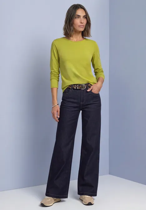 Eine Frau trägt ein leuchtend grünes Oberteil und weite schwarze Jeans.