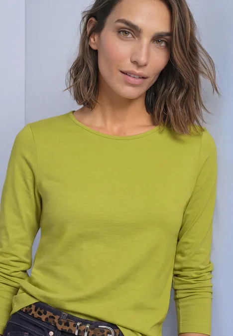Eine Frau mit kurzem braunen Haar trägt einen grasgrünen Pullover und eine Hose mit Leopardenmuster.